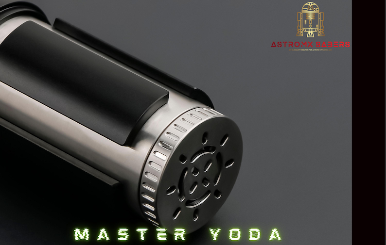 May include: A close-up of a silver and black lightsaber hilt. The hilt has a cylindrical design with a black grip and a detailed end cap. The text "MASTER YODA" is displayed in green, stylized lettering.