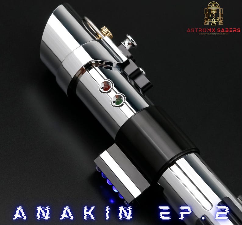 May include: A silver and black lightsaber with red and green buttons, and the text "ANAKIN EP. 2" in blue. The lightsaber has a metallic finish and is angled against a dark background. The logo "ASTROMX SABERS" is in the upper right corner.