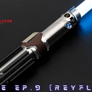 May include: A silver and brown lightsaber with a glowing blue blade. The hilt features a brown leather grip and black accents. The text "LUKE EP.9 (REYFLEX)" is at the bottom of the image. The Astromx Sabers logo is in the upper left corner.