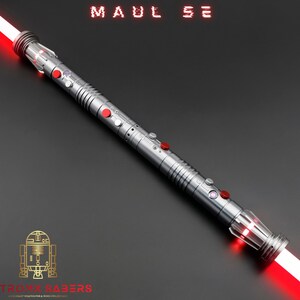 Op de afbeelding: Een zilveren lichtzwaard met een rood lemmet, met rode en zilveren knoppen en accenten. De tekst "MAUL SE" wordt bovenaan weergegeven en het Astro Sabers-logo staat onderaan. Het lichtzwaard staat schuin tegen een donkergrijze achtergrond.
