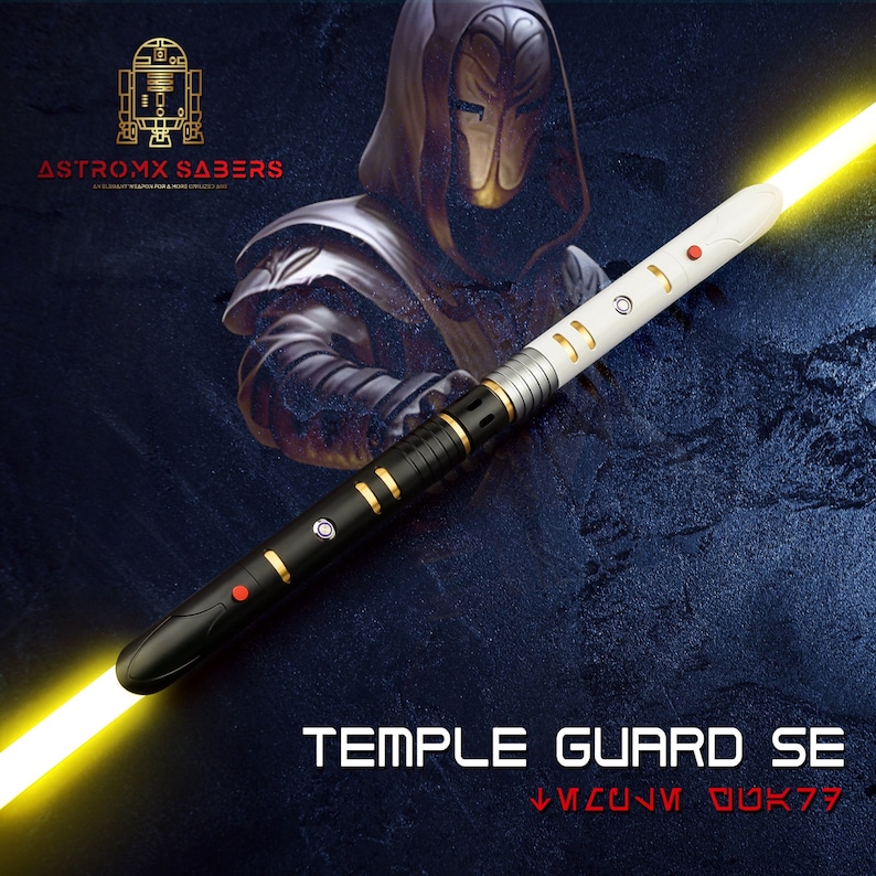 K&ouml;nnte beinhalten: Ein schwarz-wei&szlig;-goldenes Lichtschwert mit gelber Klinge, mit dem Text "TEMPLE GUARD SE" und der Marke "ASTROMX SABERS". Das Lichtschwert hat ein schlankes Design mit roten und goldenen Akzenten.