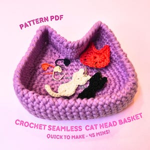 Può includere: Un cestino a forma di testa di gatto viola all'uncinetto con un design senza cuciture. Il cestino contiene orecchini e segnapunti a forma di gatto bianco, nero e rosso. Il testo sull'immagine recita "Pattern PDF" e "Crochet Seamless Cat Head Basket".