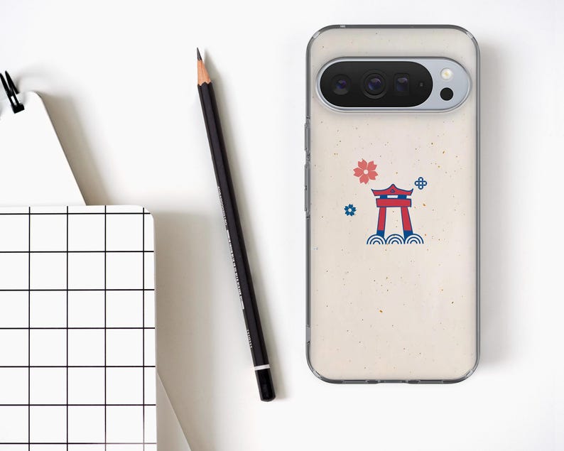 Puede incluir: Una funda transparente para tel&eacute;fono con un dise&ntilde;o de inspiraci&oacute;n japonesa. La funda presenta un fondo beige con una puerta torii roja, una flor rosa y detalles azules. Un l&aacute;piz negro y un bloc de notas con un patr&oacute;n de cuadr&iacute;cula tambi&eacute;n est&aacute;n en la imagen.