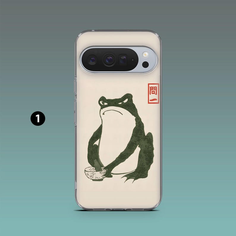 Op de afbeelding: Telefoonhoesje met een illustratie van een groene kikker die een kom vasthoudt, met Japanse tekst in een rood vierkant. De kikker heeft een boze uitdrukking. De hoes is gebroken wit met een transparante rand.