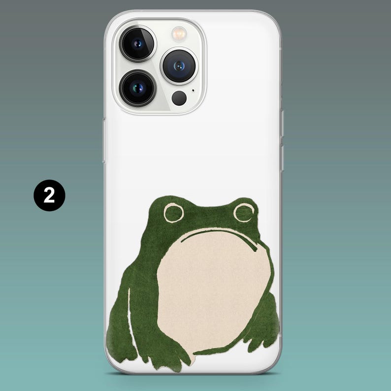 Pode incluir: Capa de telem&oacute;vel branca com uma ilustra&ccedil;&atilde;o de um sapo verde. O sapo tem uma barriga bege clara e olhos grandes e redondos. A capa tem uma borda transparente e um recorte para a c&acirc;mara na parte superior. O n&uacute;mero "2" est&aacute; no canto superior esquerdo.