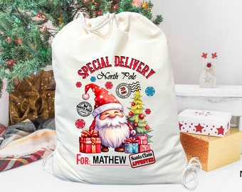 May include: A white canvas Santa sack with a red and white Santa Claus illustration, a Christmas tree, and the text "Special Delivery North Pole For: MATHEW Santa Claus Approved".