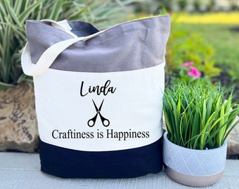 May include: A tri-color tote bag with a gray, white, and black design. The bag has a white panel with the name "Linda" and the text "Craftiness is Happiness" with a pair of scissors graphic.