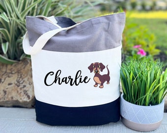 May include: A grey and black canvas tote bag with a white panel featuring the name "Charlie" and a cartoon dachshund.