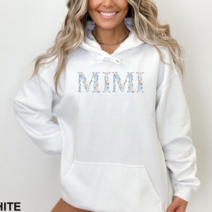May include: White hoodie with the word "MIMI" in floral print across the chest. The text is in a light blue, pink, and white floral pattern. The word "WHITE" is printed at the bottom of the image.