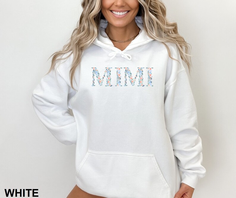 May include: White hoodie with the word "MIMI" in floral print across the chest. The text is in a light blue, pink, and white floral pattern. The word "WHITE" is printed at the bottom of the image.