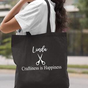May include: Black tote bag with white text that reads "Linda" with a pair of scissors and "Craftiness is Happiness".