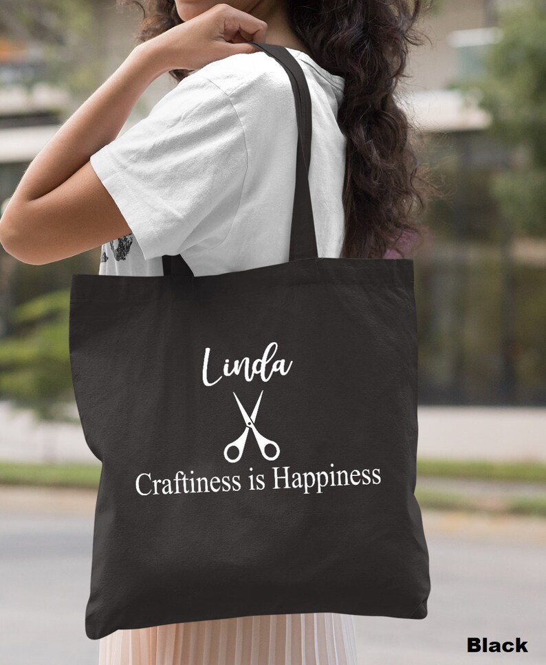 May include: Black tote bag with white text that reads "Linda" with a pair of scissors and "Craftiness is Happiness".