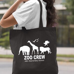 May include: Black canvas tote bag with white silhouette images of a giraffe, elephant, lion, and birds. The text "Zoo Crew" and "ABC Elementary School" is printed in white.