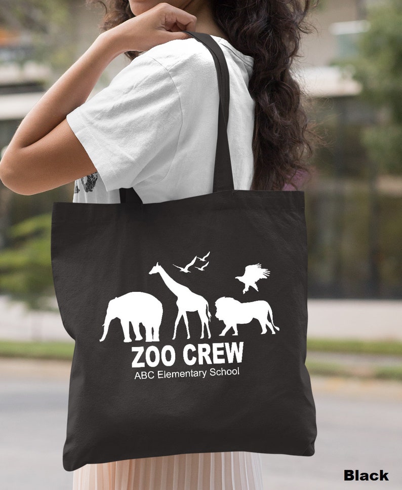 May include: Black canvas tote bag with white silhouette images of a giraffe, elephant, lion, and birds. The text "Zoo Crew" and "ABC Elementary School" is printed in white.