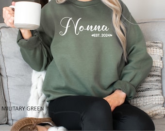 May include: A military green sweatshirt with the text "Nonna Est. 2024" in white lettering.