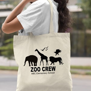 May include: A natural canvas tote bag with black silhouettes of animals, including an elephant, giraffe, lion, and birds. The text "Zoo Crew" and "ABC Elementary School" is printed in black.
