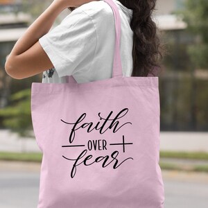Może przedstawiać: Jasnor&oacute;żowa torba typu tote z napisem "faith over fear" w czarnym, ozdobnym piśmie.