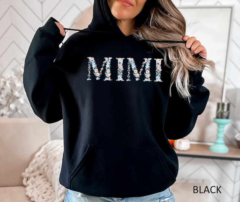May include: Black hooded sweatshirt with the word "MIMI" in floral print across the chest. The letters are filled with a pattern of small blue, pink, and white flowers. The word "BLACK" is printed in white at the bottom right.