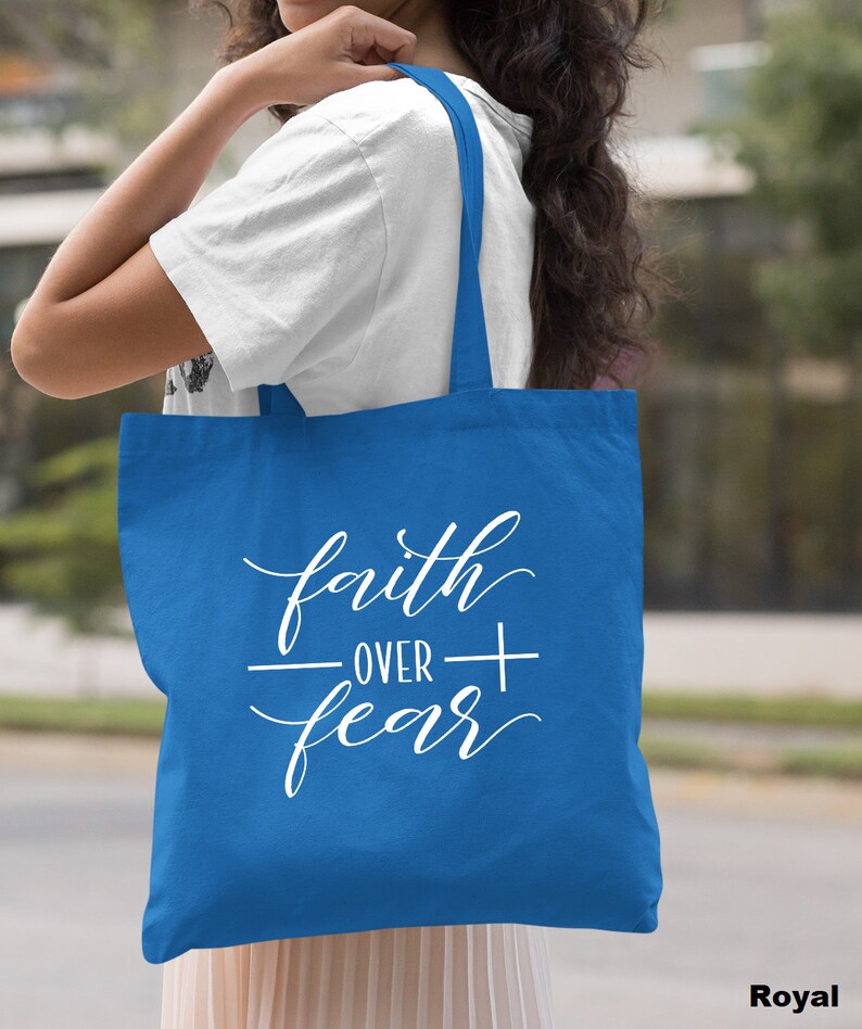 Może przedstawiać: Jasnoniebieska torba typu tote z białym napisem "faith over fear" i symbolem krzyża.