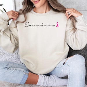 May include: A cream colored sweatshirt with the word "Survivor" and a pink ribbon printed on the front.