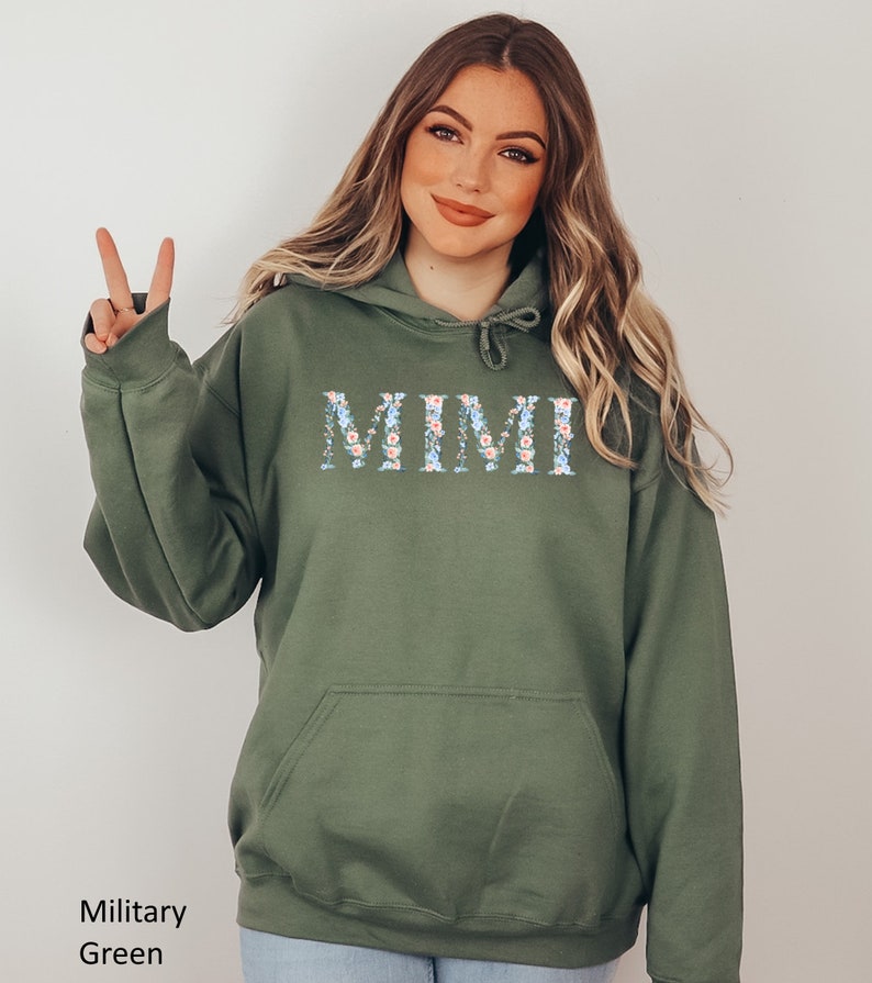 May include: Military green hoodie with the word "MIMI" in a floral design across the chest. The hoodie has a drawstring hood and a front pocket. The text "Military Green" is at the bottom left.
