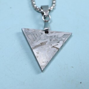 Puede incluir: Un collar con un colgante triangular de plata con superficie texturizada, que cuelga de una cadena de plata.