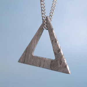 Peut inclure: Un collier avec un pendentif en forme de triangle argenté à surface texturée. Le pendentif est suspendu à une chaîne en argent.