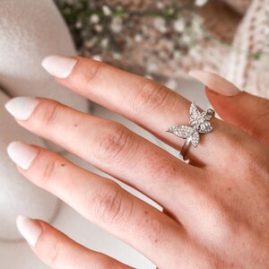 May include: A silver ring with a butterfly design featuring clear sparkling stones. The butterfly has a pearl in the centre.