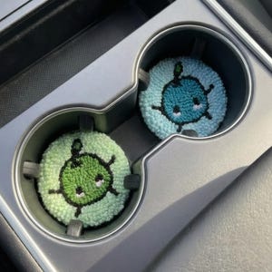 Könnte beinhalten: Zwei Untersetzer für Getränkehalter im Auto. Einer ist hellblau mit einem dunkelblauen Cartoon-Design, der andere hellgrün mit einem dunkelgrünen Cartoon-Design. Die Untersetzer sind rund und aus einem weichen, strukturierten Material.