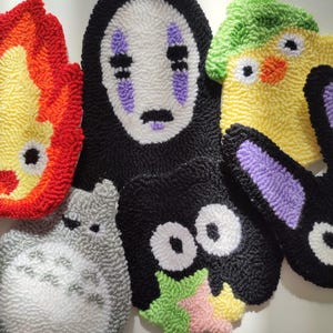 May include: Five colorful handmade plush toys featuring characters from popular animated films. The toys are made with yarn and feature embroidered details. The characters include No Face from Spirited Away, Totoro from My Neighbor Totoro, Kiki's Delivery Service, and a yellow chick.