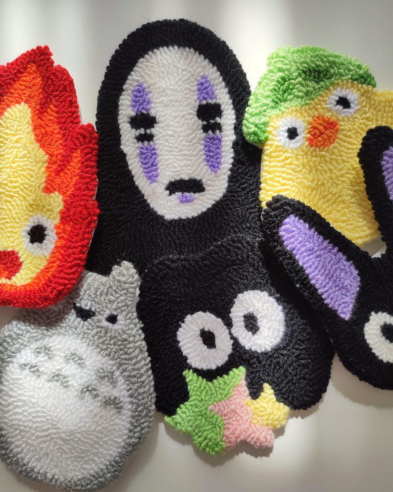 May include: Five colorful handmade plush toys featuring characters from popular animated films. The toys are made with yarn and feature embroidered details. The characters include No Face from Spirited Away, Totoro from My Neighbor Totoro, Kiki's Delivery Service, and a yellow chick.