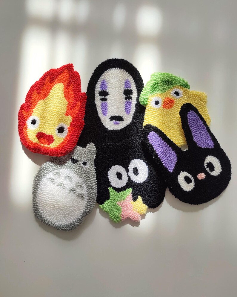 May include: Five colorful, hand-stitched felt characters from the popular animated film Studio Ghibli. The characters include No Face, Totoro, Jiji, Calcifer, and a yellow chick.