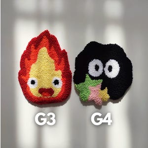 May include: Two handmade felt wall decorations. The first is a red, yellow, and orange flame with a smiling face. The second is a black, green, and pink creature with two large white eyes. The decorations are labeled G3 and G4.
