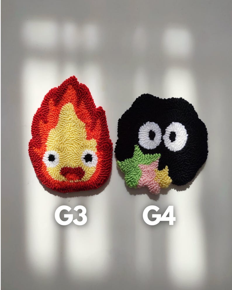 May include: Two handmade felt wall decorations. The first is a red, yellow, and orange flame with a smiling face. The second is a black, green, and pink creature with two large white eyes. The decorations are labeled G3 and G4.