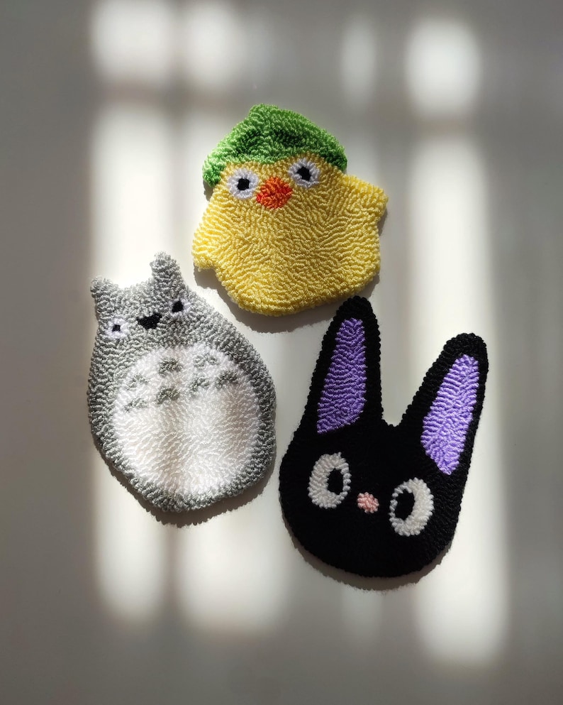 May include: Three handmade plush toys: a grey and white Totoro, a black and purple Jiji, and a yellow chick with a green hat.