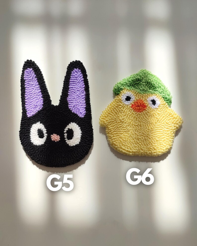 May include: Two handmade plush toys, one black cat with purple ears and white eyes, and one yellow chick with a green hat and orange beak. The toys are labeled G5 and G6.