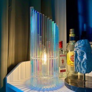 Puede incluir: Una lámpara de vidrio iridiscente arcoíris con una bombilla transparente sobre una superficie blanca. Dos botellas de licor están sobre la superficie, una con la etiqueta "Beefeater London" y la otra con la etiqueta "Havana Club".