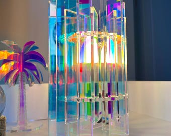 May include: A modern, iridescent acrylic lamp with a geometric design. The lamp features vertical and horizontal rectangular panels that reflect a spectrum of colors. The lamp is a decorative lighting fixture, perfect for a contemporary home.