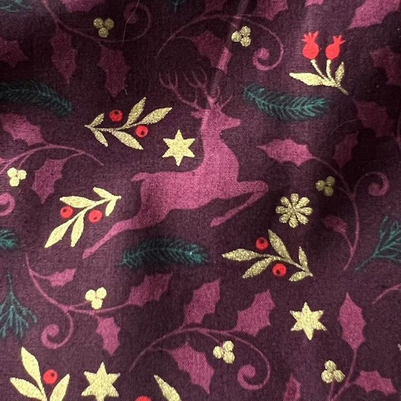 May include: A burgundy fabric with a repeating pattern of gold reindeer, holly, berries, and stars. The fabric has a soft, textured feel.
