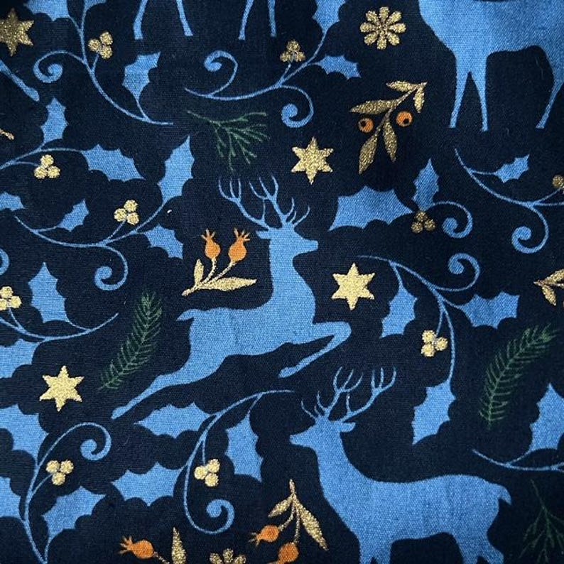 May include: Blue and gold fabric with a repeating pattern of stylized reindeer, stars, and floral designs. The background is dark blue and the reindeer are light blue.