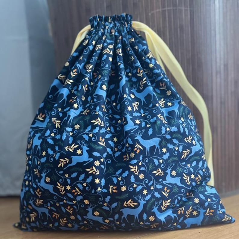 May include: A blue and gold drawstring bag with a reindeer and holly pattern. The bag is made of fabric and has a yellow drawstring.