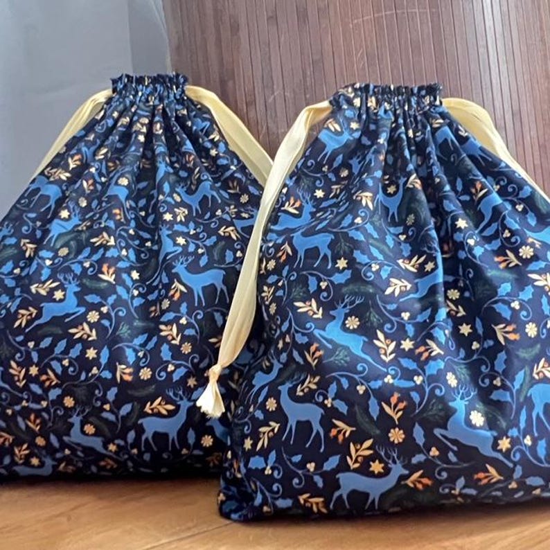 May include: Two blue drawstring bags with a gold and blue floral pattern featuring deer. The bags have yellow drawstrings.