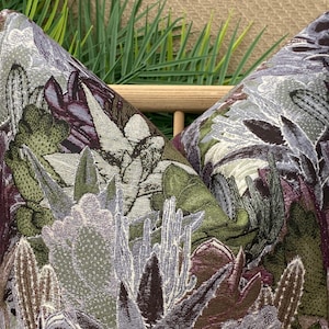 May include: Two decorative throw pillows with a floral pattern featuring a variety of green, purple, and white flowers. The pillows are made of a textured fabric that resembles embroidery.