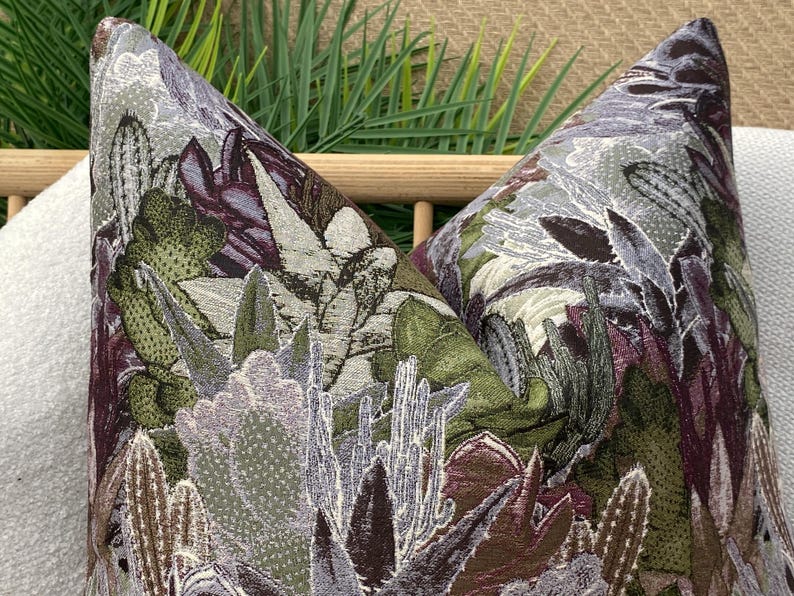 May include: Two decorative throw pillows with a floral pattern featuring a variety of green, purple, and white flowers. The pillows are made of a textured fabric that resembles embroidery.