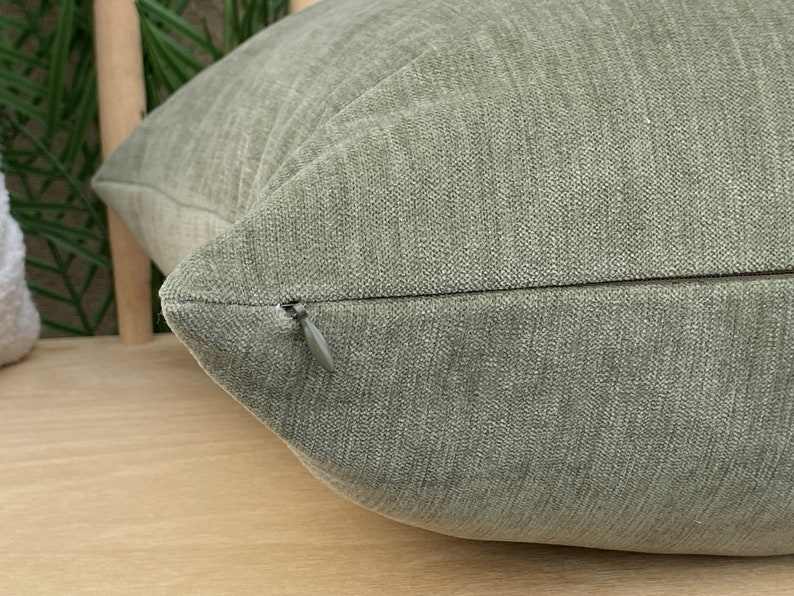 May include: Close-up of a green pillow with a zipper closure. The pillow is made of a soft, textured fabric.