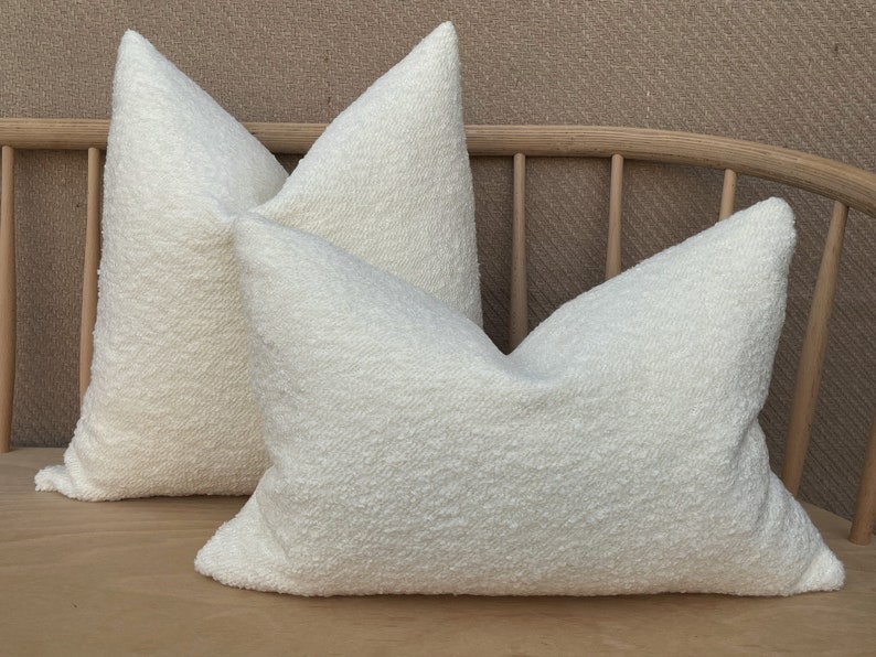 May include: Two white fluffy throw pillows with a textured surface. The pillows are arranged on a wooden bench.