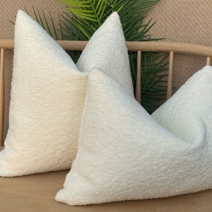 May include: Two white fluffy throw pillows on a wooden bench. The pillows are made of a soft, textured fabric.