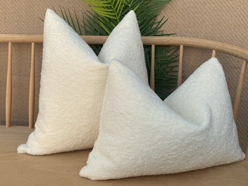 May include: Two white fluffy throw pillows on a wooden bench. The pillows are made of a soft, textured fabric.