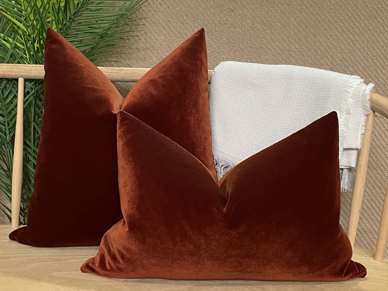 Peut inclure: Trois coussins en velours de couleur rouille dispos&eacute;s sur un banc en bois. Les coussins sont tous de la m&ecirc;me taille et de la m&ecirc;me forme, et ils ont un toucher doux et luxueux.