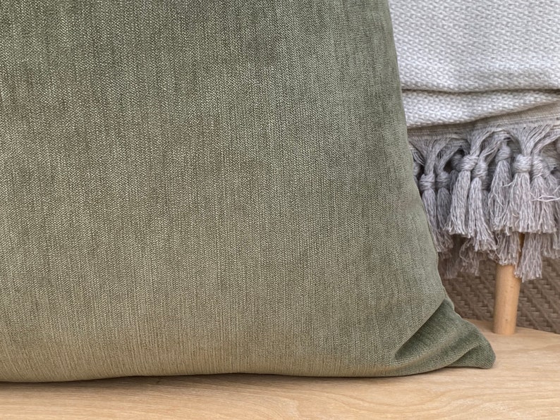 May include: A soft, green velvet pillow with a subtle texture. The pillow is shown on a light wood surface.